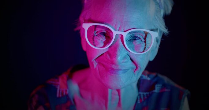 A smiling Asian women who is an elderly woman, likes to have fun, be in a good sense of humor, showing off her friendly gesture to the people amidst the colorful of festival light at night.