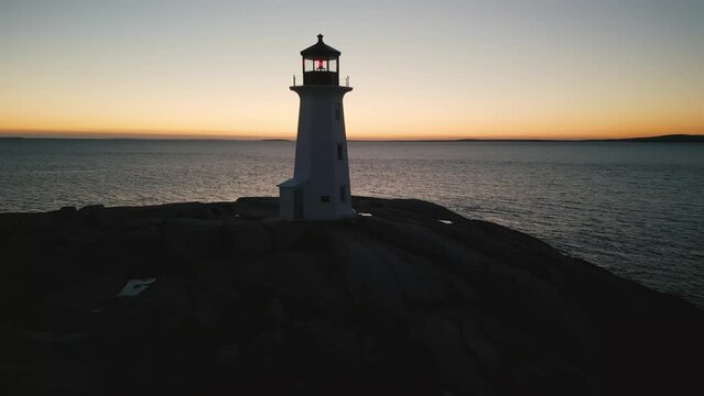 Cinematic shot of a drone on Peggy's Cove Lighthouse at dusk Atlantic Coast Halifax Nova Scotia Canada. Aerial view of an ancient lighthouse at dusk on the shore of a rocky landscape.