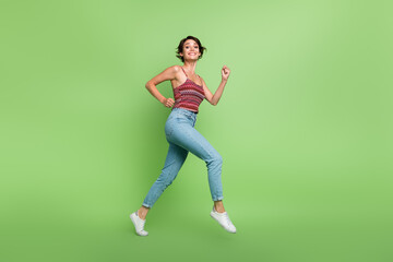 Fototapeta na wymiar Full length photo of good mood cheerful girl wear stylish clothes running jogging going empty space isolated on green color background