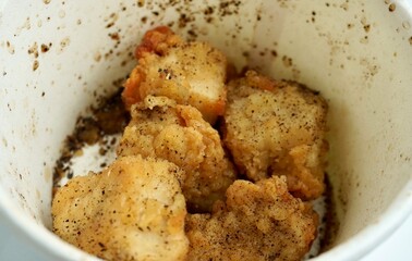 Deep crispy air fried chicken meat with thin skin. Savory snacks with salt and black peppers. Delicious food photography isolated on horizontal ratio white paper bowl background.