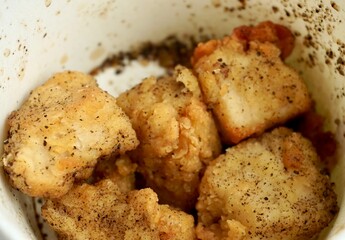 Deep crispy air fried chicken meat with thin skin. Savory snacks with salt and black peppers. Delicious food photography isolated on horizontal ratio white paper bowl background.