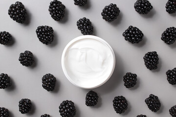Container with bodycare and skincare cream on a grey background with blackberries. Cosmetic facial skin care and spa. Natural treatment concept.