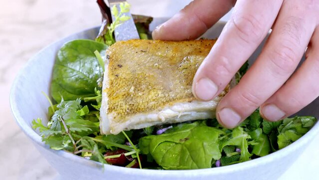 The chef serves a portion with salad and white fish. Fried zander and salad. Food preparation. Slow motion footage.