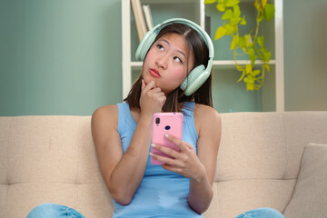 Beautiful woman thinking with hand on chin and headphones listening to music on sofa happy shopping...