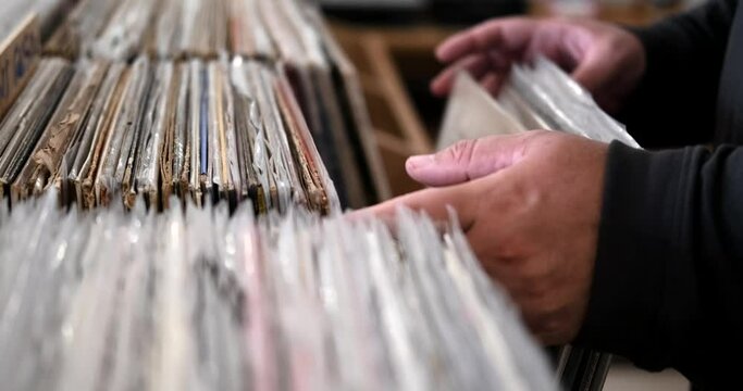 Close-up of a man hands choosing a vinyl record from a large selection in a cozy vintage store. Classical and rock music in analogue sound. Music lover shopping at a vintage market.