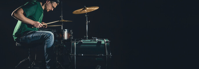 A male drummer plays a drum kit on a black background, copy space.