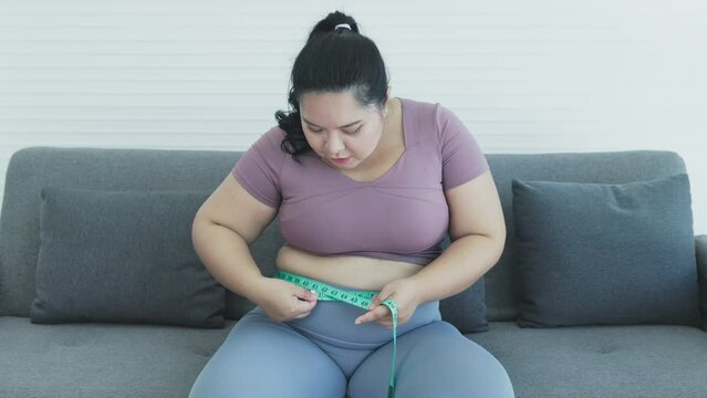 chuuby woman sitting on sofa using tape to measure her waist circumference