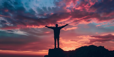 A man stands with open arms atop a cliff under a mesmerizing sky, symbolizing freedom and achievement