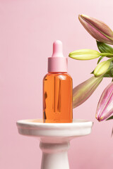 Glass dropper bottle on podium with lily flowers on pink background. Hyaluronic acid oil, serum with collagen and peptides skin care product. Cosmetic liquid mockup in bottle.
