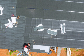 With help an air nail gun, professional roofing contractor installs new asphalt bitumen shingles on...
