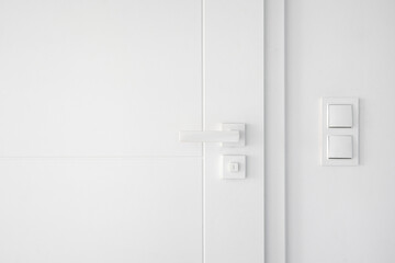 Light switches on white wall near closed room door with mechanical handle