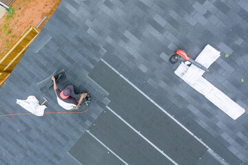 Professional roofing contractor uses an air nail gun to install new asphalt bitumen shingles on...