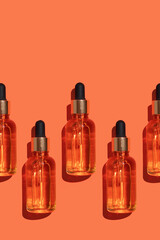 Seamless pattern of anti aging serum in glass bottle with dropper on orange background. Creative layout, cosmetic seamless pattern, flat lay. Creative cosmetics pattern background