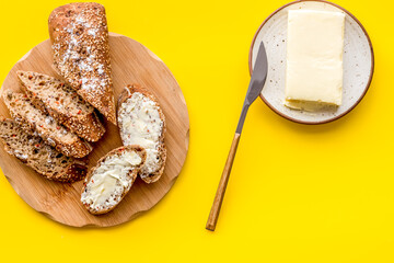 Traditional breakfast. Wholegrain bread on cutting board with butter on plate on yellow background top view