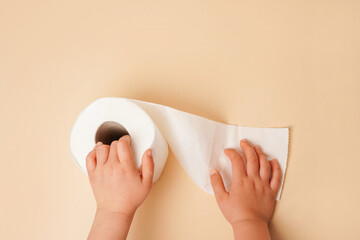 Roll of white toilet paper in child hands. beige background with copy space