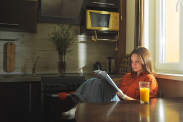 Beautiful young woman reading in the kitchen at home.
