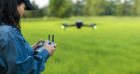 A female farmer wearing a hat stands and controls a drone in a green wheat field. Modern technology...