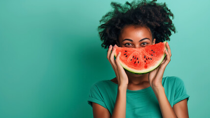 beautiful smiling black woman with curly hair in green tshirt holding watermelon slice covering her...