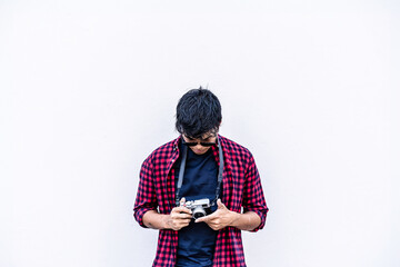 Photographer checks vintage camera, framed by blank space. Millennial embracing photography in urban setting. Retro-inspired hobby captured in modern city. Total white background.