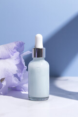 Serum with floral extracts for skincare. Nature cosmetics in glass bottle with pipette and iris flowers on blue background. Face and body care spa concept.