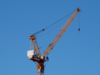 Fototapeta na wymiar a yellow construction crane at a high rise construction site on a clear blue sky