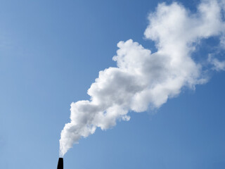 a plume of smoke or steam from an industrial smokestack on a clear blue sky