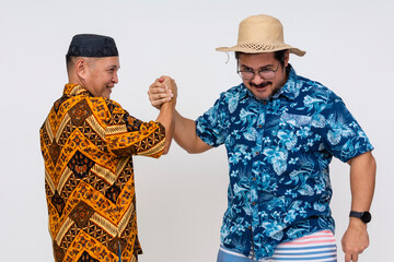 A middle-aged Indonesian man in batik and kopiah in a playful arm wrestling bout with a tourist in...