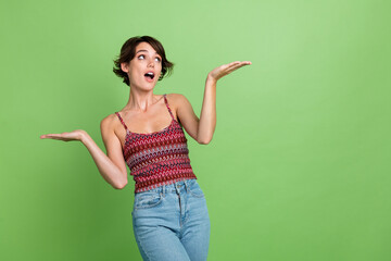 Photo of excited adorable girl wear trendy clothes hold empty space news banner isolated on green color background