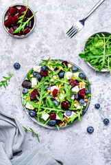Healthy useful salad with beetroot, blueberries, feta cheese, arugula and walnuts, gray table background, top view