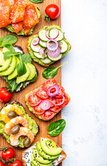Avocado toasts with salmon, shrimp, vegetables, spinach, capers and cream cheese, served on wooden board, white table background, top view - 791860883