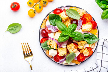 Salad with tomatoes, stale bread, onion, mozzarella cheese, green basil and olive oil, white table background, top view - 791861673