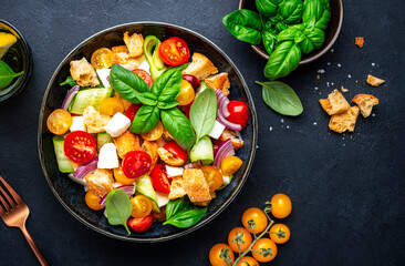 Frash vegetable salad with stale bread, tomatoes, cucumber, cheese, onion, olive oil, sea salt and green basil, black table background, top view