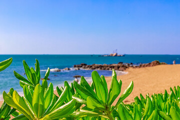 View of the shore of the South China Sea with a sandy beach, palm trees and plants, large stones. China