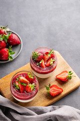 Panna cotta with strawberry and cream in glasses with fresh berries on a wooden board on a gray background with napkin.
