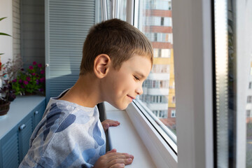 A cute boy looks out the window of a balcony and smile. The boy is standing near the window with...