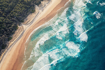 Foamy ocean waves roll and approach sandy beach. Majesty turquoise seascape. Top view from a drone.