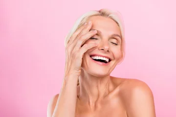Foto auf Acrylglas Photo of happy lovely cute retired woman applying nourishing lotion for skin health isolated on pink color background © deagreez