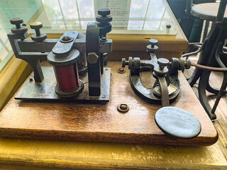 Antique telegraph for sending Morse code in the early days of telecommunication, on display in an office mock-up at a living history museum, for motifs of Americana, technology, and preservation © Kenneth