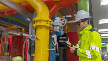 Asian engineer wearing glasses working in the boiler room,maintenance checking technical data of...