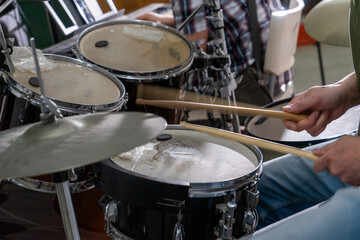 Close-up of a man's hands playing drums. His drumsticks hit with energy, showing the rhythm and motion of live performance. Cymbals and drumheads are slightly blurred, indicating movement.