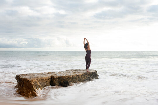 woman free swimmer doing stretching exercise on a rock before entering the sea.