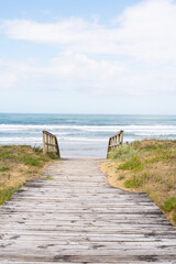 Wooden walkway to reach the beach, sea in the background of the image.