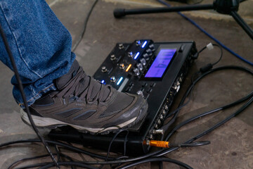 A foot steps on a guitar effects pedal, captured from the side. The shoe is a simple sneaker, and...