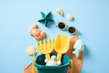Bucket with sand molds, beach towel, and sunglasses on a blue background. Flat lay, top view.