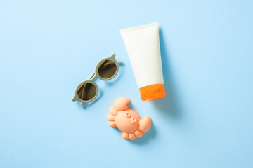 Flat lay sunscreen lotion tube, kids sunglasses and crab sandbox toy on beige table. Infant skin care, sun protection concept.