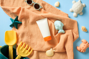 Flat lay sunscreen lotion tube, kids sunglasses and sand molds on blue background. Infant skin care, sun protection concept.