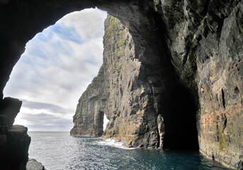 Rocks and caves of the coast near the famous spireTrøllkonufingur  towering rock formation on...