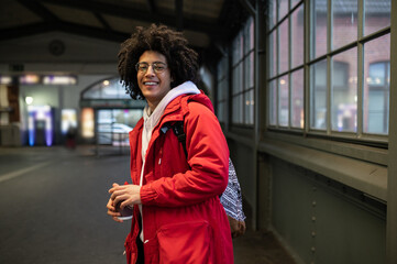 Curly-haired young guy at the railway platform with a coffee cup in hands
