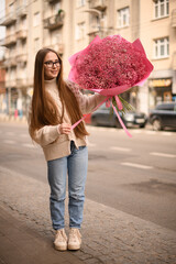 Street photo of a girl in knitted sweater holding bouquet of pink flowers