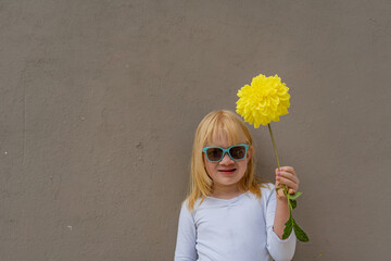 niña albina usando gafas y mirando al frente mientras sostiene una flor amarilla en sus manos 